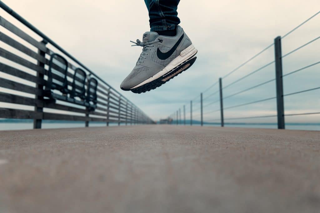 Man jumping in the air on a bridge wear Nike trainers