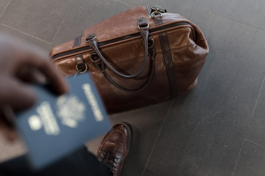 A person holding a passport in the foreground and luggage in the background